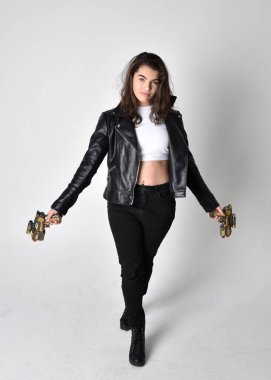 Uzun boylu, kahverengi saçlı, ceketli, siyah deri elbiseli, açık renk stüdyo arka planında duran genç bir kadının portresi..