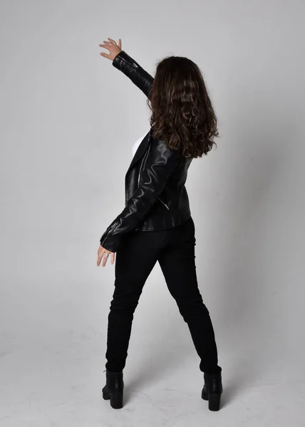 自然な茶色の髪を持つ若い女性の完全な長さの肖像画 ジャケットと黒革のScifi衣装を身に着けています カメラに背を向けて立ちポーズ ライトスタジオの背景に — ストック写真