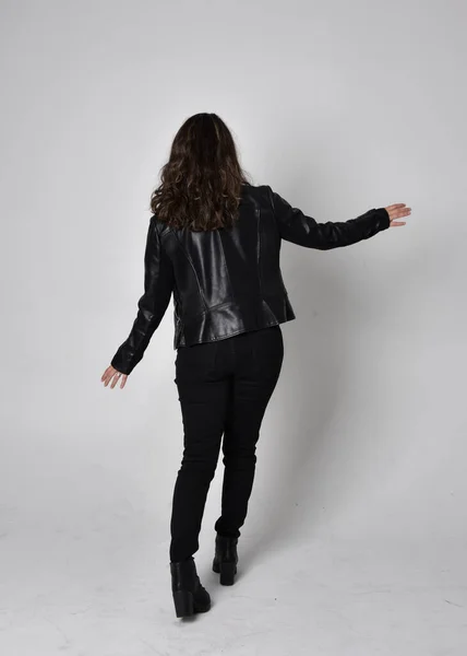 自然な茶色の髪を持つ若い女性の完全な長さの肖像画 ジャケットと黒革のScifi衣装を身に着けています カメラに背を向けて立ちポーズ ライトスタジオの背景に — ストック写真