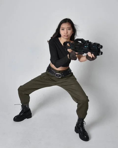 全长肖像漂亮的黑发 亚洲女孩穿着黑色上衣和卡其布军裤和皮靴 举着科幻小说枪 孤立无援的特工 背景浅灰色 — 图库照片