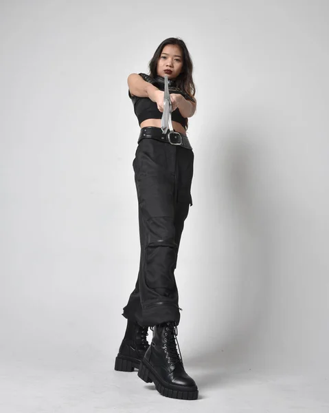 全长肖像漂亮的年轻亚洲女孩穿着黑色的坦克顶部 实用的裤子和皮靴 拿着剑站在那里 与工作室的背景隔离 — 图库照片