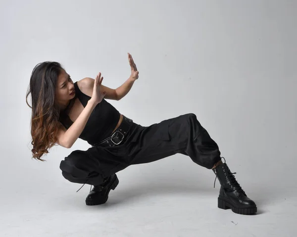 stock image Full length portrait of pretty young asian girl wearing black tank top, utilitarian  pants and leather boots. Sitting poseisolated against a  studio background.