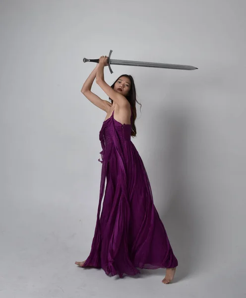 全长肖像漂亮的黑发亚洲女孩穿着紫色飘逸的礼服 拿着剑站在工作室的背景上 — 图库照片