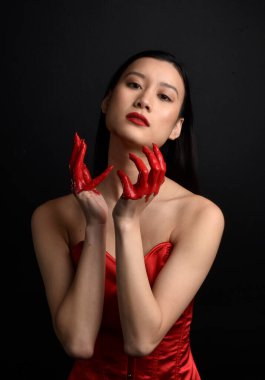 Kırmızı korse giyen güzel Asyalı bir kadının yakın plan portresi, kanlı boyayla kaplanmış, Gotik korku tarzında, yaratıcı el hareketleriyle koyu siyah stüdyo arka planına izole edilmiş..