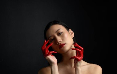 Kırmızı korse giyen güzel Asyalı bir kadının yakın plan portresi, kanlı boyayla kaplanmış, Gotik korku tarzında, yaratıcı el hareketleriyle koyu siyah stüdyo arka planına izole edilmiş..