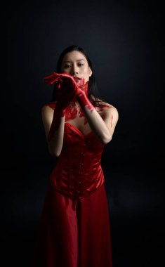 Kırmızı korse giyen güzel Asyalı bir kadının yakın plan portresi, kanlı boyayla kaplanmış, Gotik korku tarzında, yaratıcı el hareketleriyle koyu siyah stüdyo arka planına izole edilmiş..