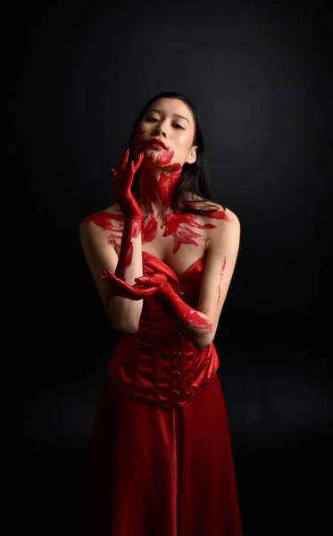 赤のコルセットを身に着けている美しい若いアジアの女性の肖像画を閉じます 黒のスタジオの背景に対して隔離された創造的な手のジェスチャーでゴシックホラースタイルでポーズ血塗られた塗料で覆われています — ストック写真