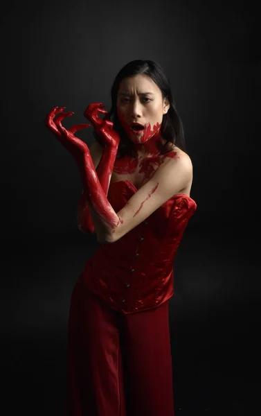 赤のコルセットを身に着けている美しい若いアジアの女性の肖像画を閉じます 黒のスタジオの背景に対して隔離された創造的な手のジェスチャーでゴシックホラースタイルでポーズ血塗られた塗料で覆われています — ストック写真
