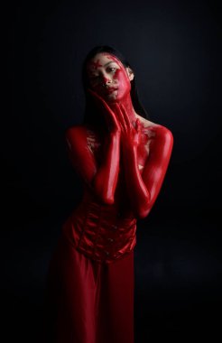 Kırmızı korse giyen güzel Asyalı bir kadının yakın plan portresi, kanlı boyayla kaplanmış, Gotik korku tarzında, yaratıcı el hareketleriyle koyu siyah stüdyo arka planına izole edilmiş..