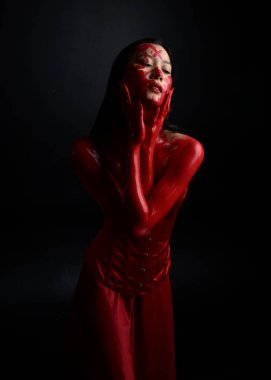 Kırmızı korse giyen güzel Asyalı bir kadının yakın plan portresi, kanlı boyayla kaplanmış, Gotik korku tarzında, yaratıcı el hareketleriyle koyu siyah stüdyo arka planına izole edilmiş..