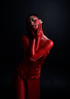 Kırmızı korse giyen güzel Asyalı bir kadının yakın plan portresi, kanlı boyayla kaplanmış, Gotik korku tarzında, yaratıcı el hareketleriyle koyu siyah stüdyo arka planına izole edilmiş..