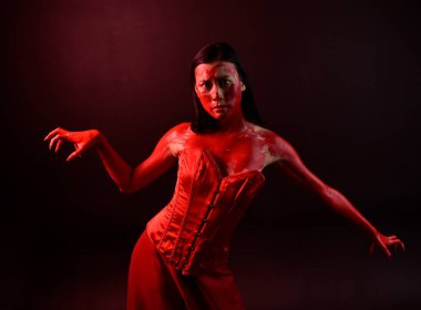 Kırmızı korse giyen güzel Asyalı bir kadının yakın plan portresi, kanlı boyayla kaplanmış, Gotik korku tarzında, yaratıcı el hareketleriyle koyu siyah stüdyo arka planına izole edilmiş..