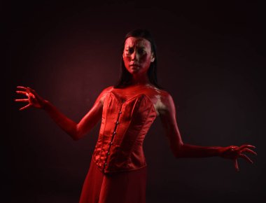 Kırmızı korse giyen güzel Asyalı bir kadının yakın plan portresi, kanlı boyayla kaplanmış, Gotik korku tarzında, yaratıcı el hareketleriyle koyu siyah stüdyo arka planına izole edilmiş..