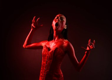 Kırmızı korse giyen güzel Asyalı bir kadının yakın plan portresi, kanlı boyayla kaplanmış, Gotik korku tarzında, yaratıcı el hareketleriyle koyu siyah stüdyo arka planına izole edilmiş..