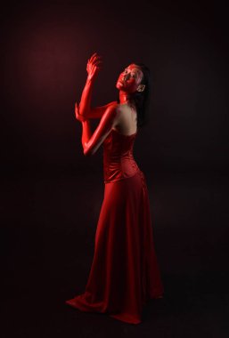 Kırmızı korse giyen güzel Asyalı bir kadının uzun boylu portresi, kanlı boyayla kaplıydı. Gotik korku pozu veriyordu. Yaratıcı el hareketleri koyu siyah stüdyo arka planında izole edilmişti..