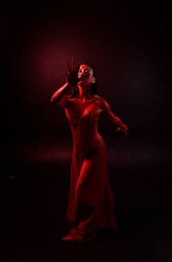 Kırmızı korse giyen güzel Asyalı bir kadının uzun boylu portresi, kanlı boyayla kaplıydı. Gotik korku pozu veriyordu. Yaratıcı el hareketleri koyu siyah stüdyo arka planında izole edilmişti..