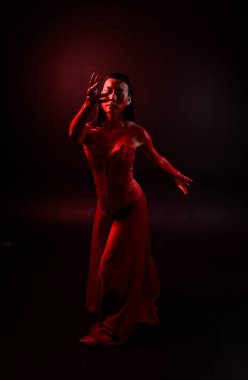 Kırmızı korse giyen güzel Asyalı bir kadının uzun boylu portresi, kanlı boyayla kaplıydı. Gotik korku pozu veriyordu. Yaratıcı el hareketleri koyu siyah stüdyo arka planında izole edilmişti..