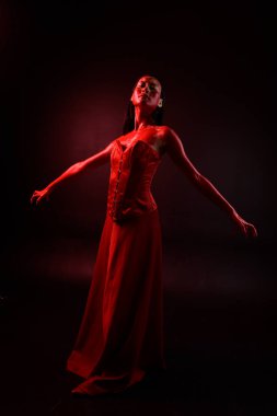 Kırmızı korse giyen güzel Asyalı bir kadının uzun boylu portresi, kanlı boyayla kaplıydı. Gotik korku pozu veriyordu. Yaratıcı el hareketleri koyu siyah stüdyo arka planında izole edilmişti..