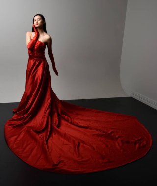 Full length  portrait of beautiful young asian woman wearing red corset, long opera gloves and ornate crown headdress. Gestural hand poses isolated on light studio background.
