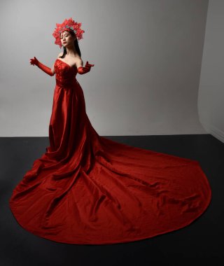 Full length  portrait of beautiful young asian woman wearing red corset, long opera gloves and ornate crown headdress. Gestural hand poses isolated on light studio background.