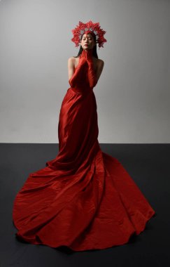 Full length  portrait of beautiful young asian woman wearing red corset, long opera gloves and ornate crown headdress. Gestural hand poses isolated on light studio background.