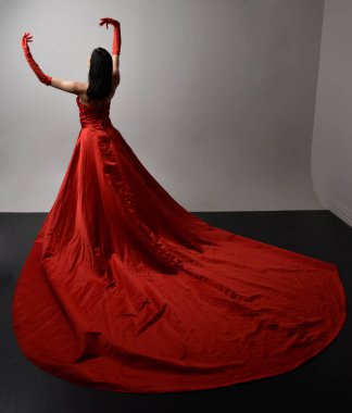 Full length  portrait of beautiful young asian woman wearing red corset, long opera gloves and ornate crown headdress. Gestural hand poses isolated on light studio background.