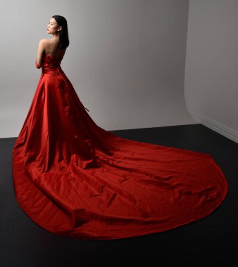 Full length  portrait of beautiful young asian woman wearing red corset, long opera gloves and ornate crown headdress. Gestural hand poses isolated on light studio background.