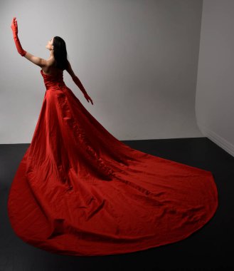Full length  portrait of beautiful young asian woman wearing red corset, long opera gloves and ornate crown headdress. Gestural hand poses isolated on light studio background.