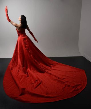 Full length  portrait of beautiful young asian woman wearing red corset, long opera gloves and ornate crown headdress. Gestural hand poses isolated on light studio background.