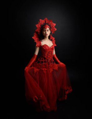 Full length  portrait of beautiful young asian woman wearing red corset, long opera gloves and ornate crown headdress. Graceful posing  isolated on light studio background.