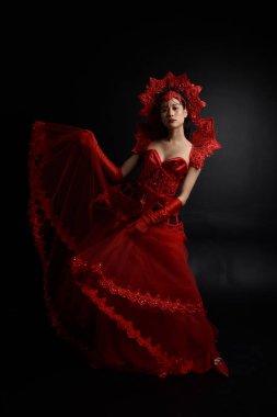 Full length  portrait of beautiful young asian woman wearing red corset, long opera gloves and ornate crown headdress. Graceful posing  isolated on light studio background.