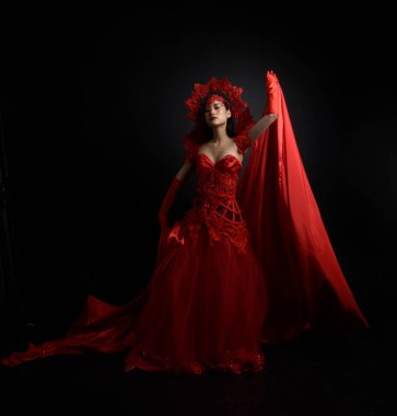 Full length  portrait of beautiful young asian woman wearing red corset, long opera gloves and ornate crown headdress. Graceful posing  isolated on light studio background.
