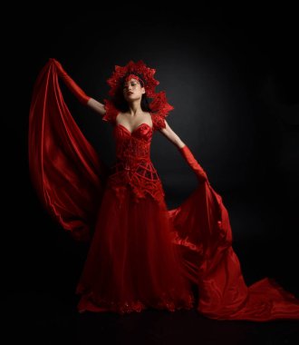 Full length  portrait of beautiful young asian woman wearing red corset, long opera gloves and ornate crown headdress. Graceful posing  isolated on light studio background.