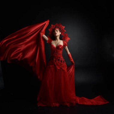 Full length  portrait of beautiful young asian woman wearing red corset, long opera gloves and ornate crown headdress. Graceful posing  isolated on light studio background.
