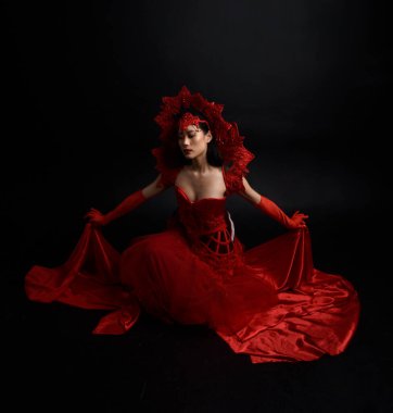 Full length  portrait of beautiful young asian woman wearing red corset, long opera gloves and ornate crown headdress. Graceful posing  isolated on light studio background.