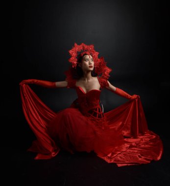 Full length  portrait of beautiful young asian woman wearing red corset, long opera gloves and ornate crown headdress. Graceful posing  isolated on light studio background.