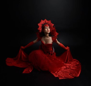 Full length  portrait of beautiful young asian woman wearing red corset, long opera gloves and ornate crown headdress. Graceful posing  isolated on light studio background.