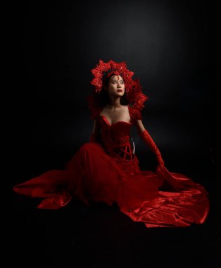 Full length  portrait of beautiful young asian woman wearing red corset, long opera gloves and ornate crown headdress. Graceful posing  isolated on light studio background.
