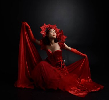 Full length  portrait of beautiful young asian woman wearing red corset, long opera gloves and ornate crown headdress. Graceful posing  isolated on light studio background.