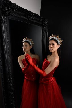 Kırmızı korse, uzun opera eldivenleri ve süslü taç başlık giyen Asyalı güzel bir kadının tam boy portresi. Stüdyonun arka planında uzun bir aynaya karşı zarif bir poz..