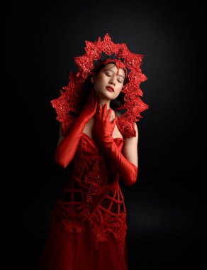 Kırmızı korse, uzun opera eldivenleri ve süslü gotik kraliçe tacı giyen güzel Asyalı bir kadının dramatik portresi. Karanlık bir stüdyo arka planında zarif bir poz..