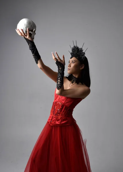 赤のコルセットと王冠を身に着けている美しい若いアジアの女性の肖像画は 暗い黒のスタジオの背景に対して隔離された創造的な手のジェスチャーでゴシックホラースタイルでポーズ — ストック写真