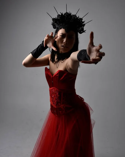 身穿红色紧身胸衣 头戴红色王冠的美丽年轻亚洲女人的肖像 以哥特式恐怖风格摆姿势 用创造性的手势与深色黑色工作室背景隔离 — 图库照片