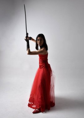 Kırmızı korse takan ve gotik kraliçe tacını takan güzel Asyalı genç bir kadının tam boy portresi. Stüdyonun arka planında zarif duruş.