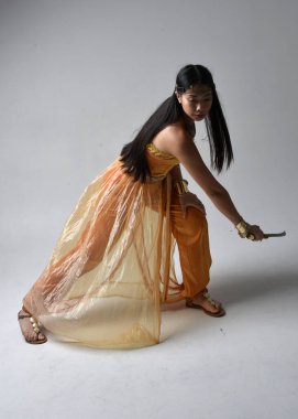 Altın Arap cübbesi giyen, stüdyo arka planında izole edilmiş, kılıç tutan, güzel Asyalı genç bir kadının portresi..