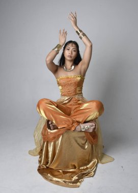 Altın Arap cübbesi giyen, stüdyo arka planında izole bir şekilde oturan, cin gibi uzun boylu Asyalı bir kadının portresi..