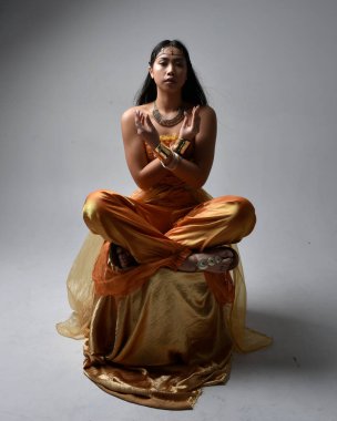 Altın Arap cübbesi giyen, stüdyo arka planında izole bir şekilde oturan, cin gibi uzun boylu Asyalı bir kadının portresi..