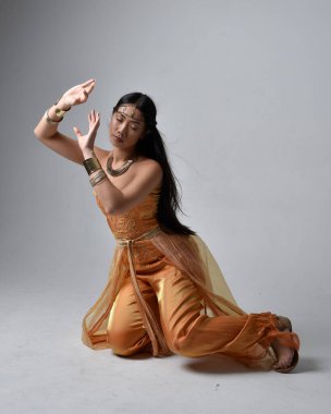 Altın Arap cübbesi giyen, stüdyo arka planında izole bir şekilde oturan, cin gibi uzun boylu Asyalı bir kadının portresi..