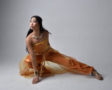 Altın Arap cübbesi giyen, stüdyo arka planında izole bir şekilde oturan, cin gibi uzun boylu Asyalı bir kadının portresi..