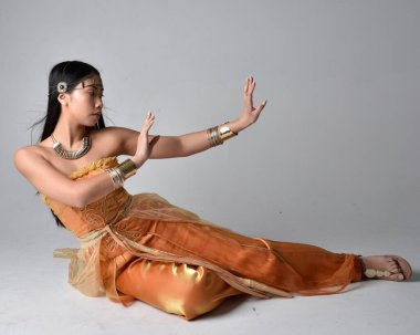 Altın Arap cübbesi giyen, stüdyo arka planında izole bir şekilde oturan, cin gibi uzun boylu Asyalı bir kadının portresi..